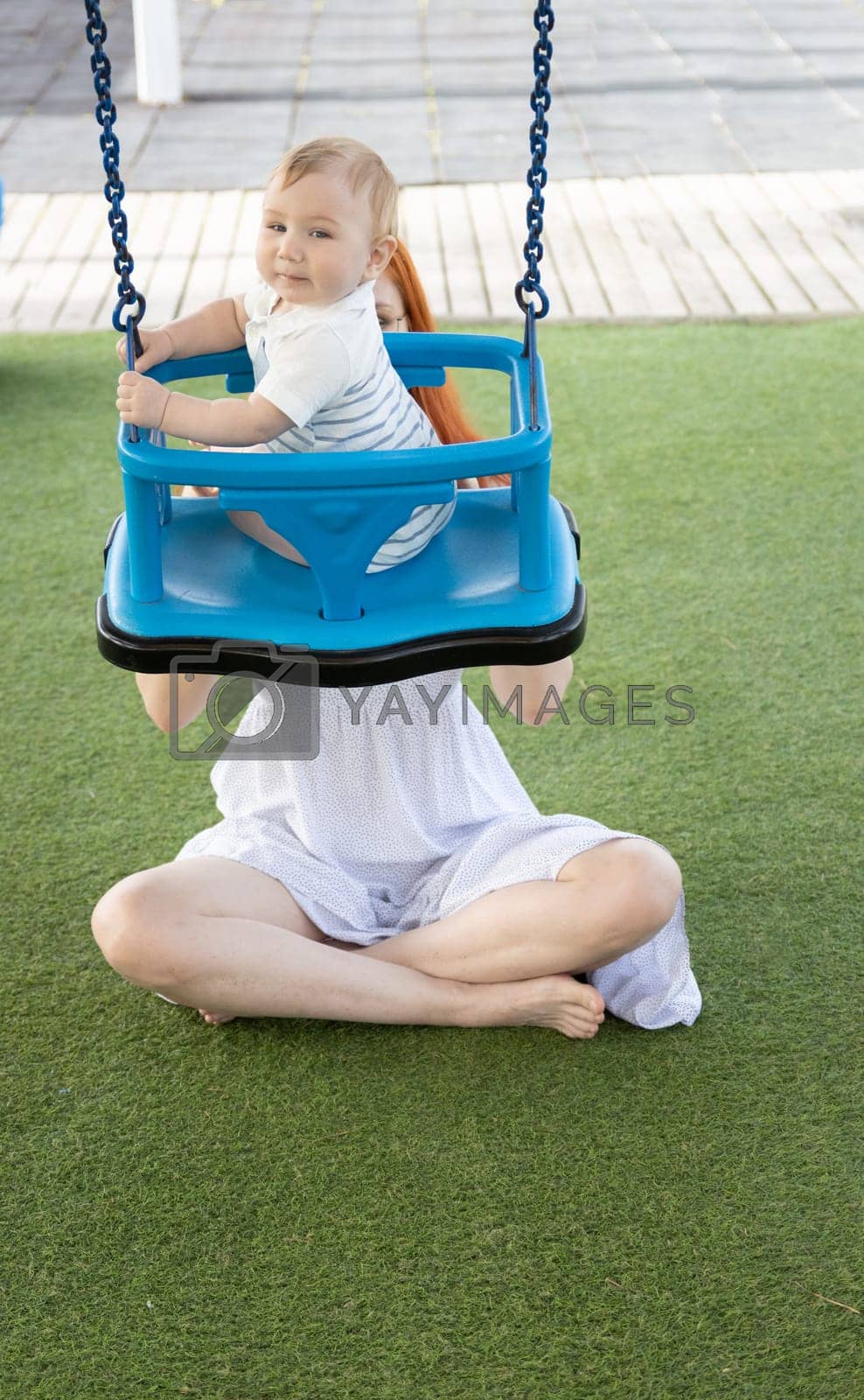 Royalty free image of Young mom shakes her young son on a swing in the playground by Studia72