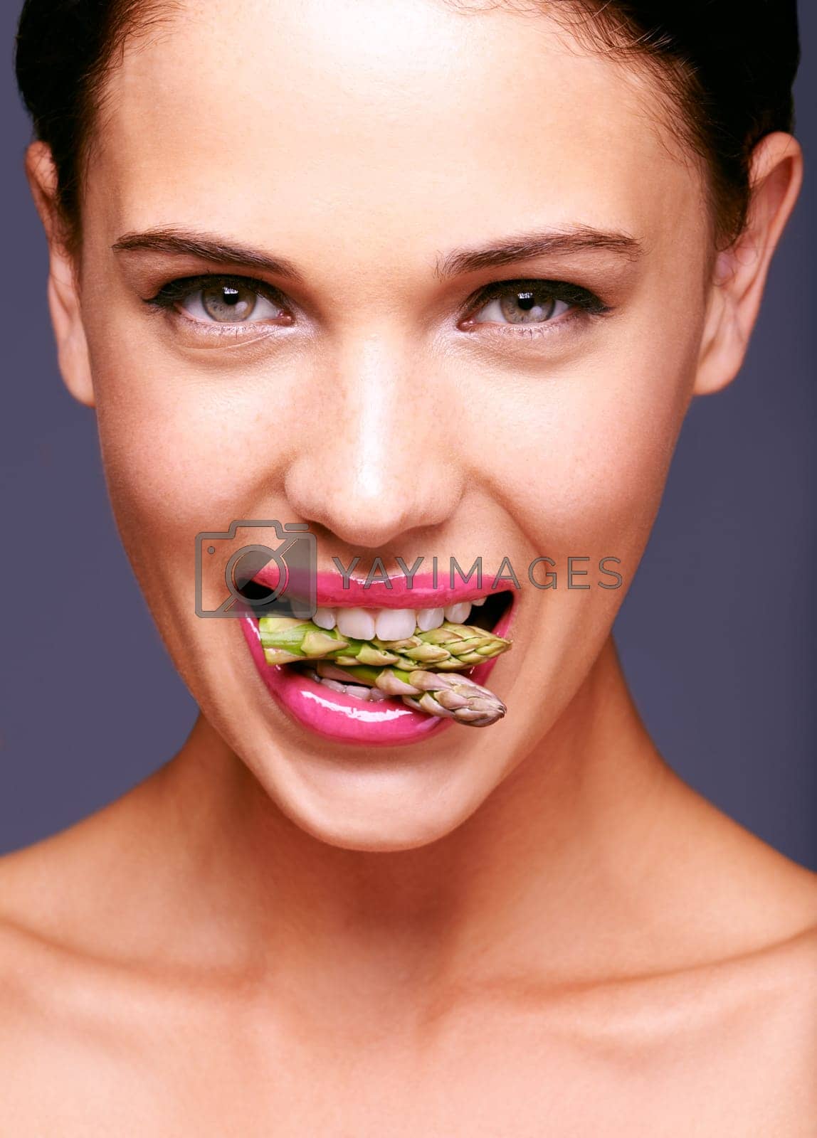 Royalty free image of Go on, eat your veggies. Portrait of a woman biting on a bunch of asparagus in studio. by YuriArcurs