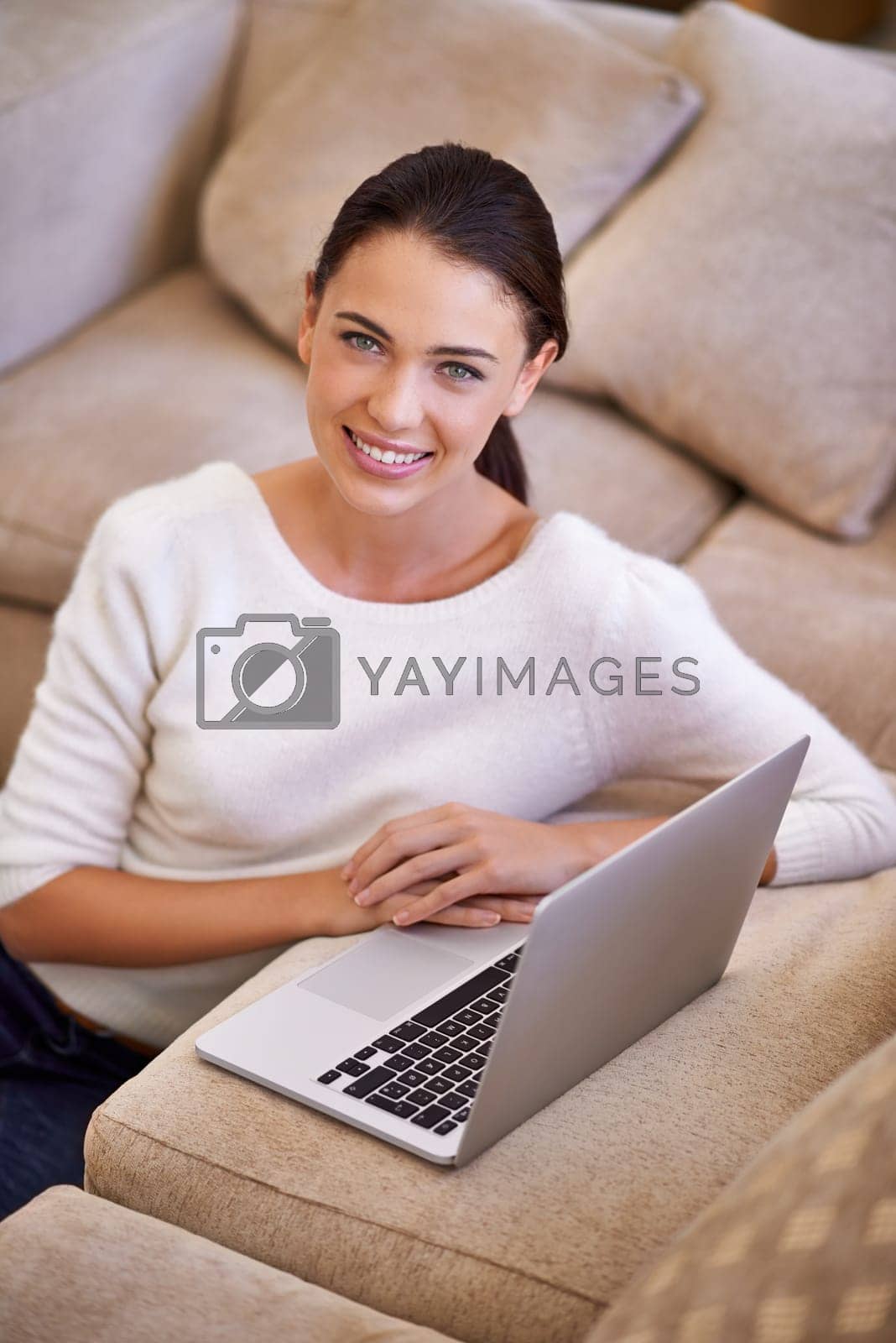 Royalty free image of Just updating my status as chilled. a young woman sitting in her living room using a laptop. by YuriArcurs