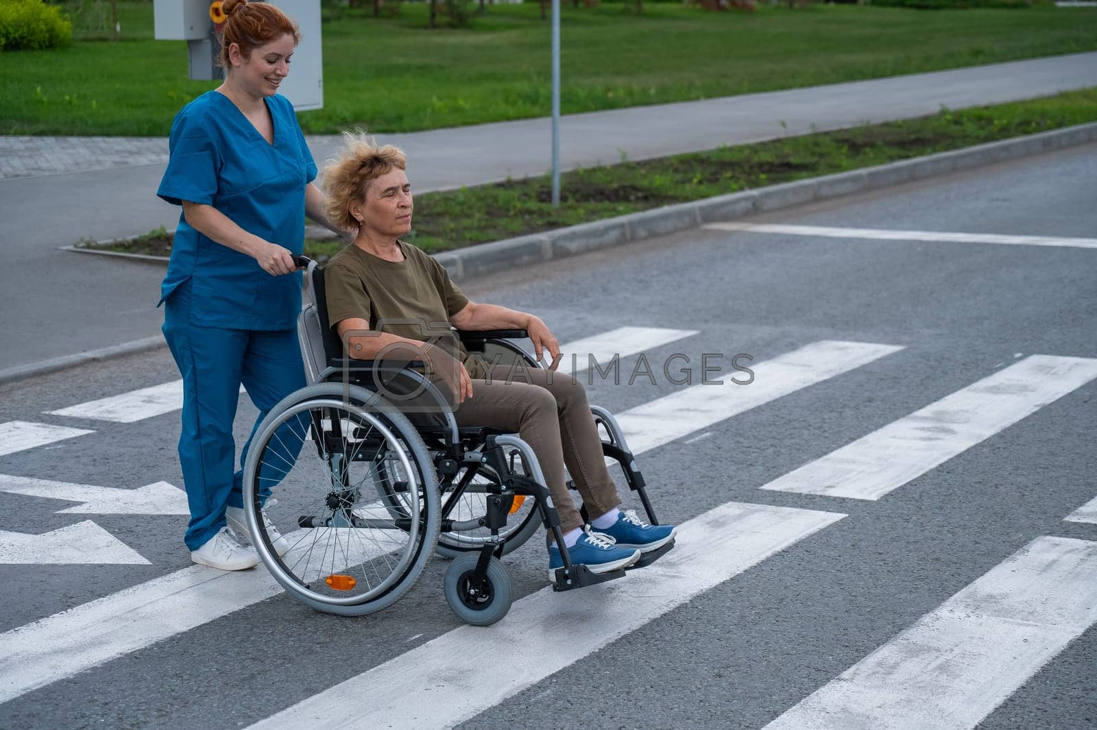 Royalty free image of Red-haired nurse pushing an elderly woman in a wheelchair across the road. by mrwed54