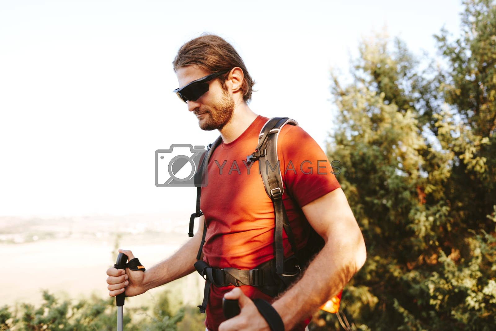 Royalty free image of Young man hiker travels through the mountains with trekking poles for nordic walking by Fabrikasimf