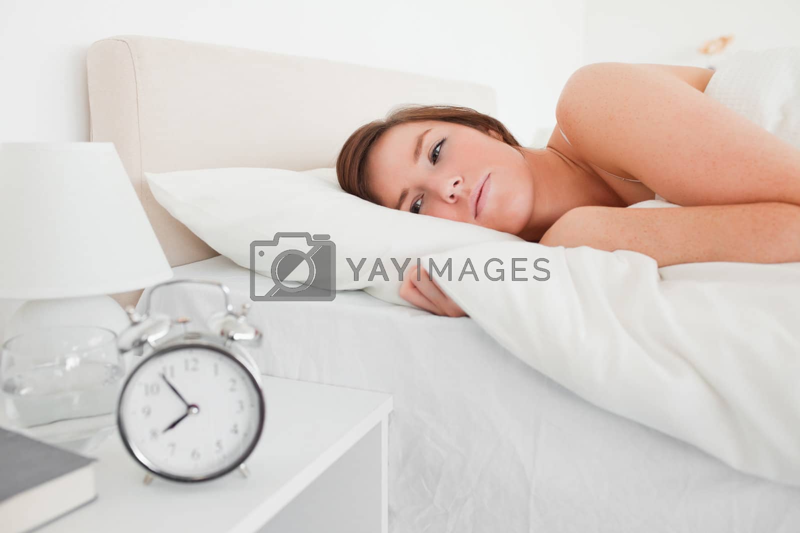Royalty free image of Beautiful brunette woman awaking with a clock while lying by Wavebreakmedia