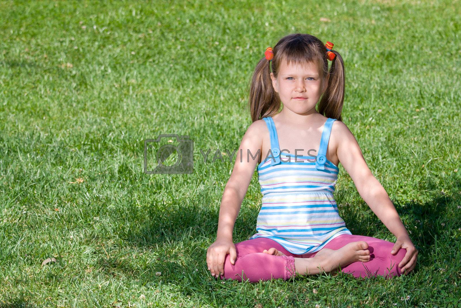 Royalty free image of Little girl sits in the shade in asana on grass by SergeyAK