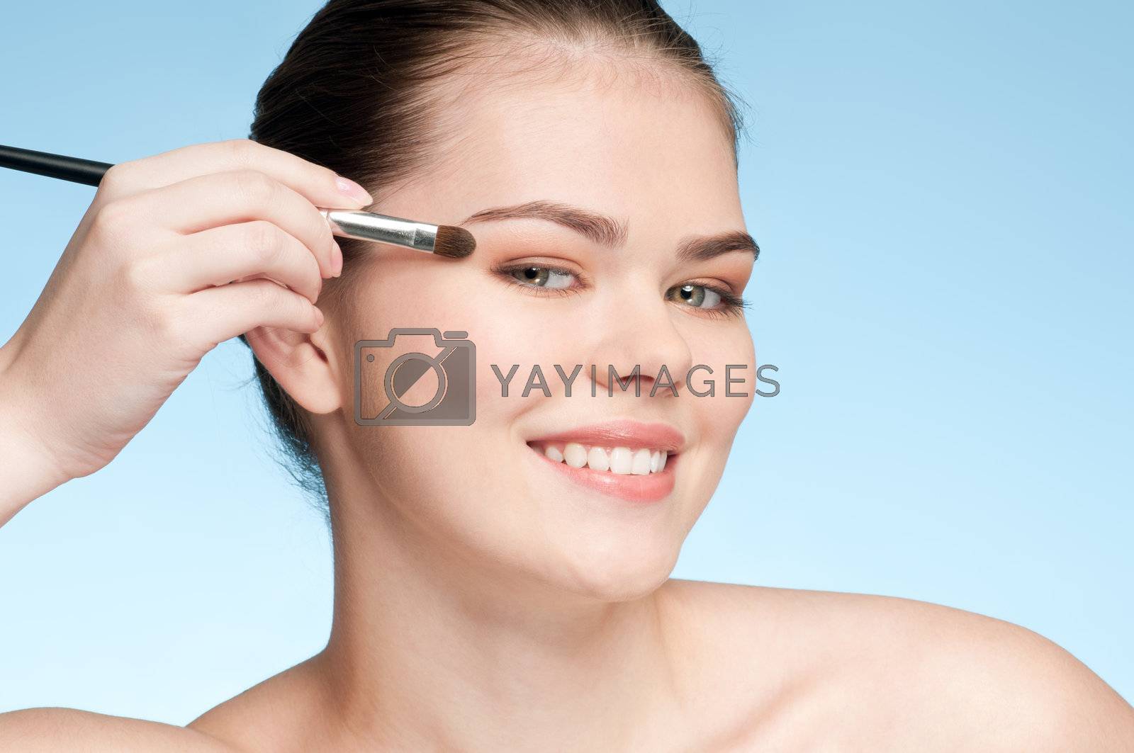Royalty free image of Beautiful young adult woman applying cosmetic shadow brush by markin