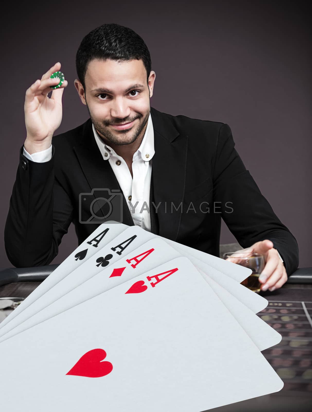 Royalty free image of Handsome gambler betting on four aces at poker table by Wavebreakmedia