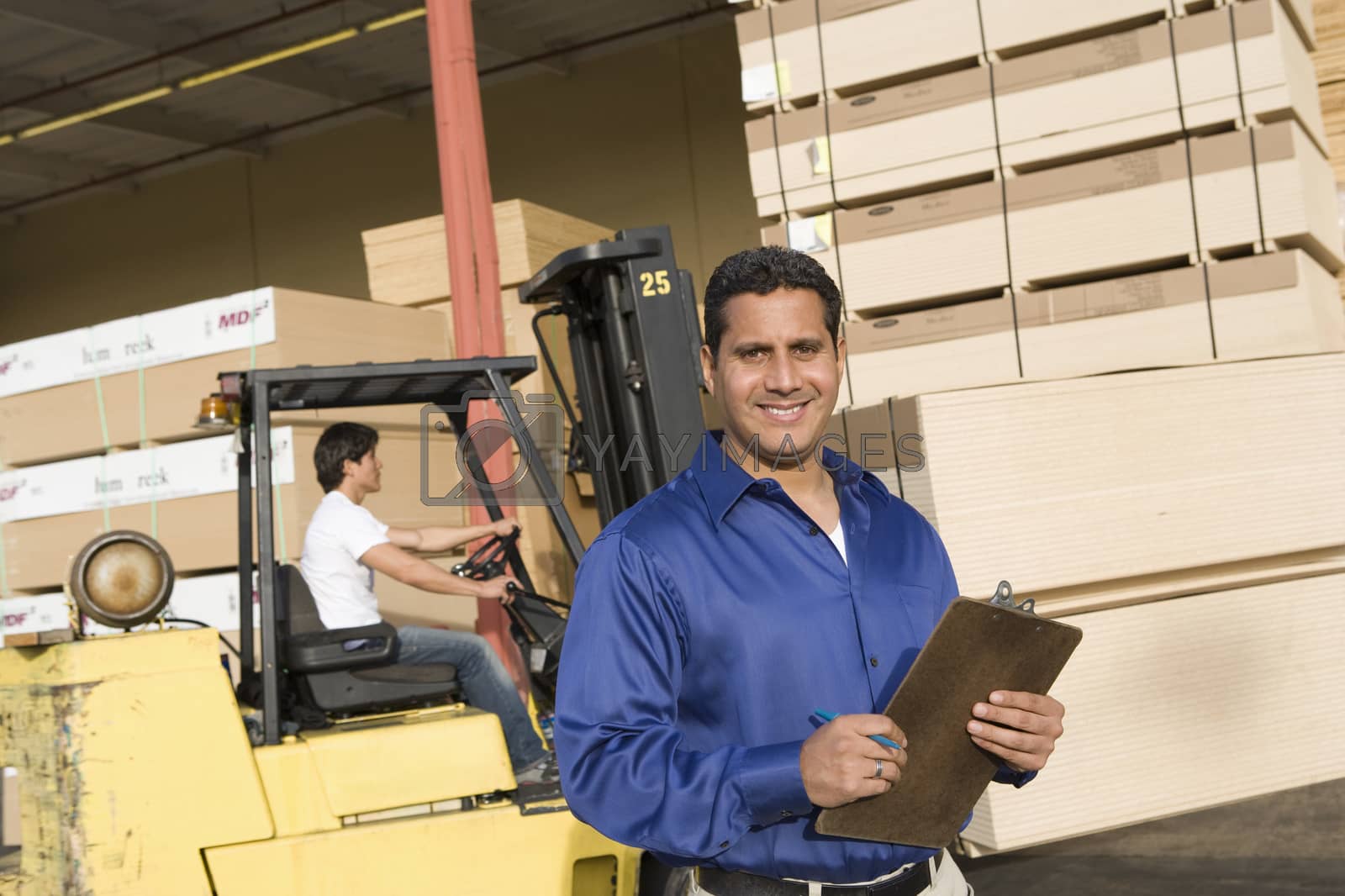 Royalty free image of Portrait of a male supervisor with clipboard and forklift truck driver in the background by moodboard