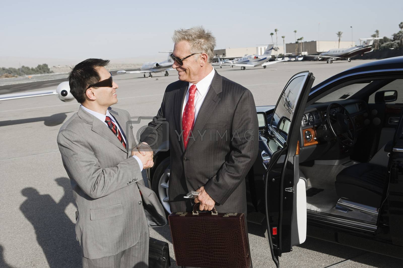 Royalty free image of Two successful businessmen shaking hands while standing by car at airfield by moodboard