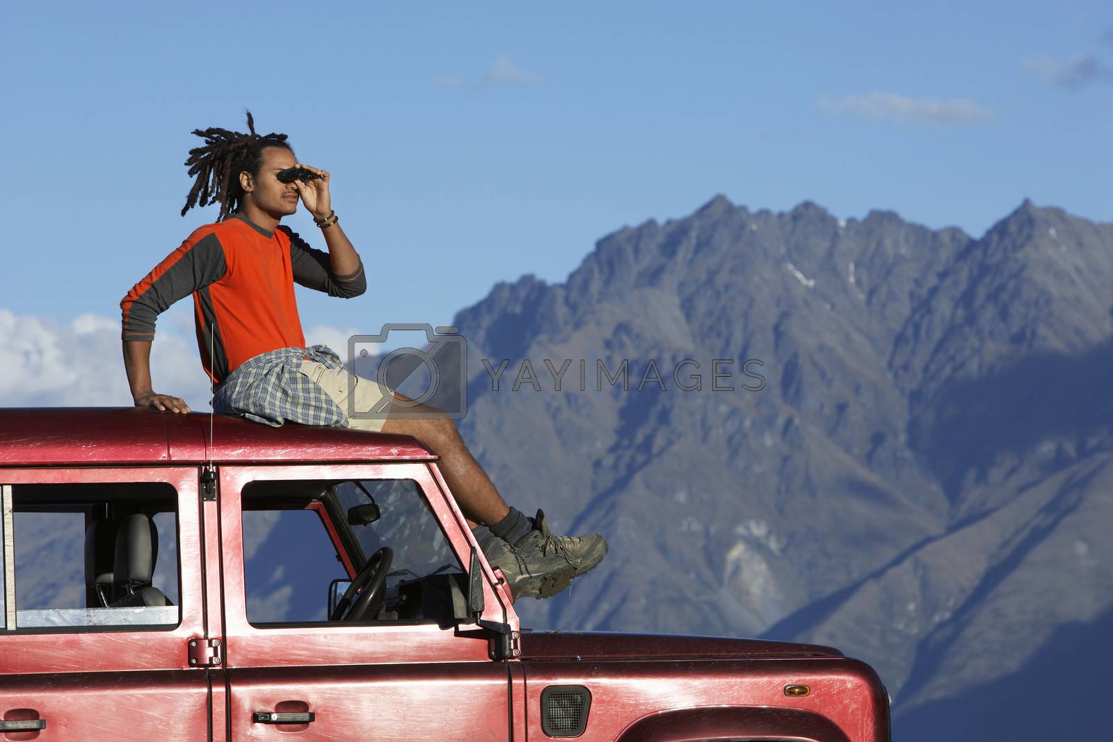 Royalty free image of Side view of a mixed race man shading eyes on top of jeep near mountains by moodboard
