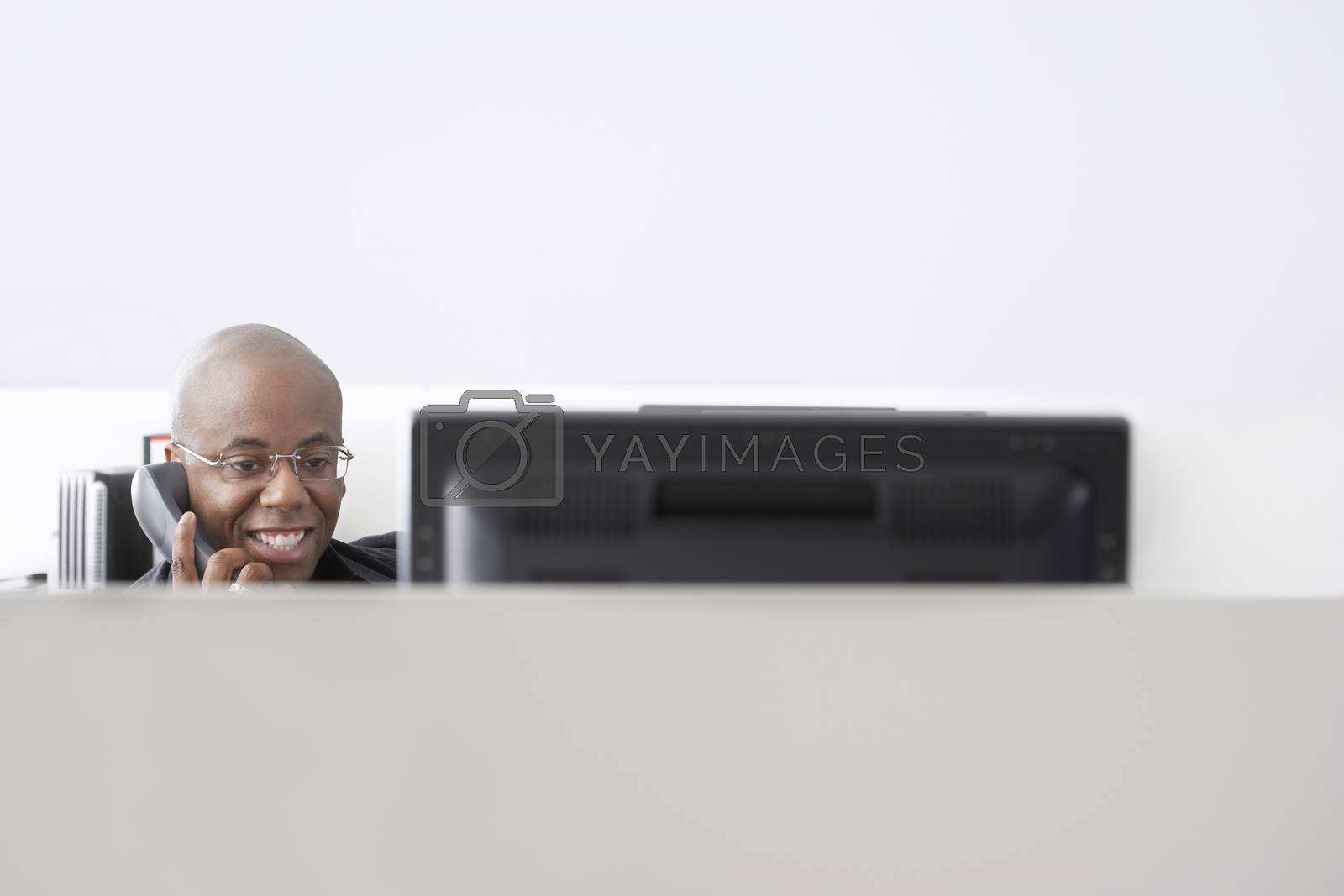 Royalty free image of Smiling African American businessman using telephone at computer desk by moodboard