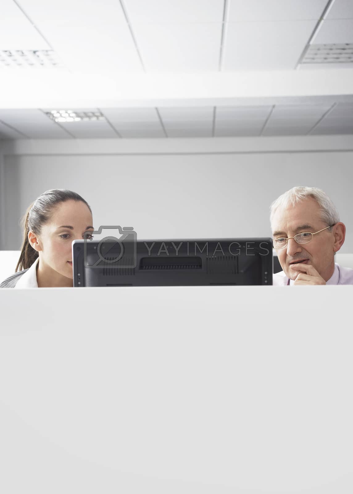 Royalty free image of Serious businesswoman and businessman looking at computer in cubicle by moodboard