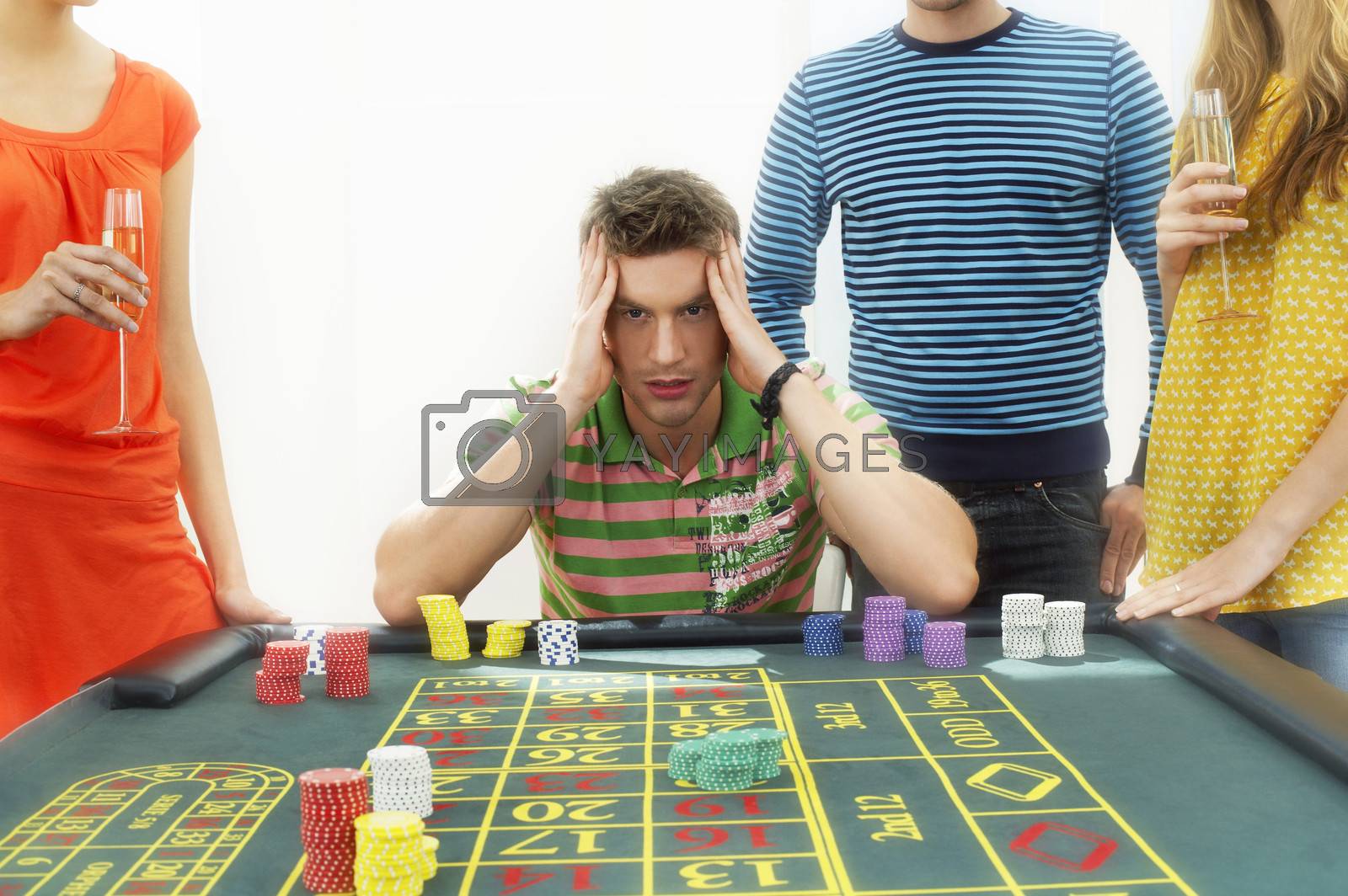 Royalty free image of Young frustrated man at roulette table with midsection of friends by moodboard