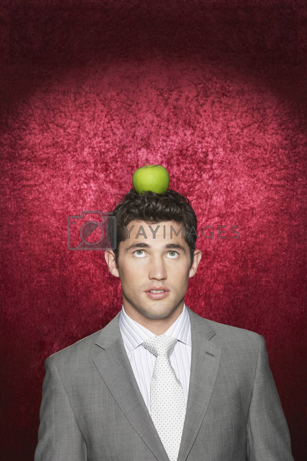 Royalty free image of Young man with apple on his head against red velvet background by moodboard