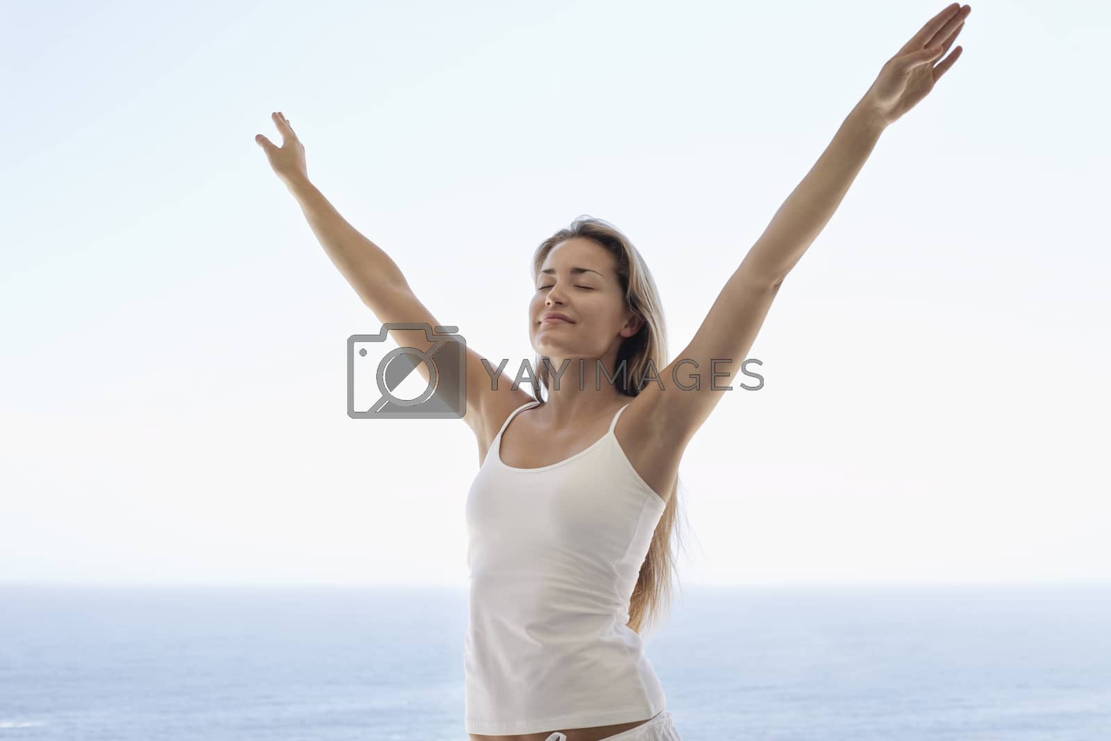 Royalty free image of Young woman with arms outstretched and eyes closed on beach by moodboard