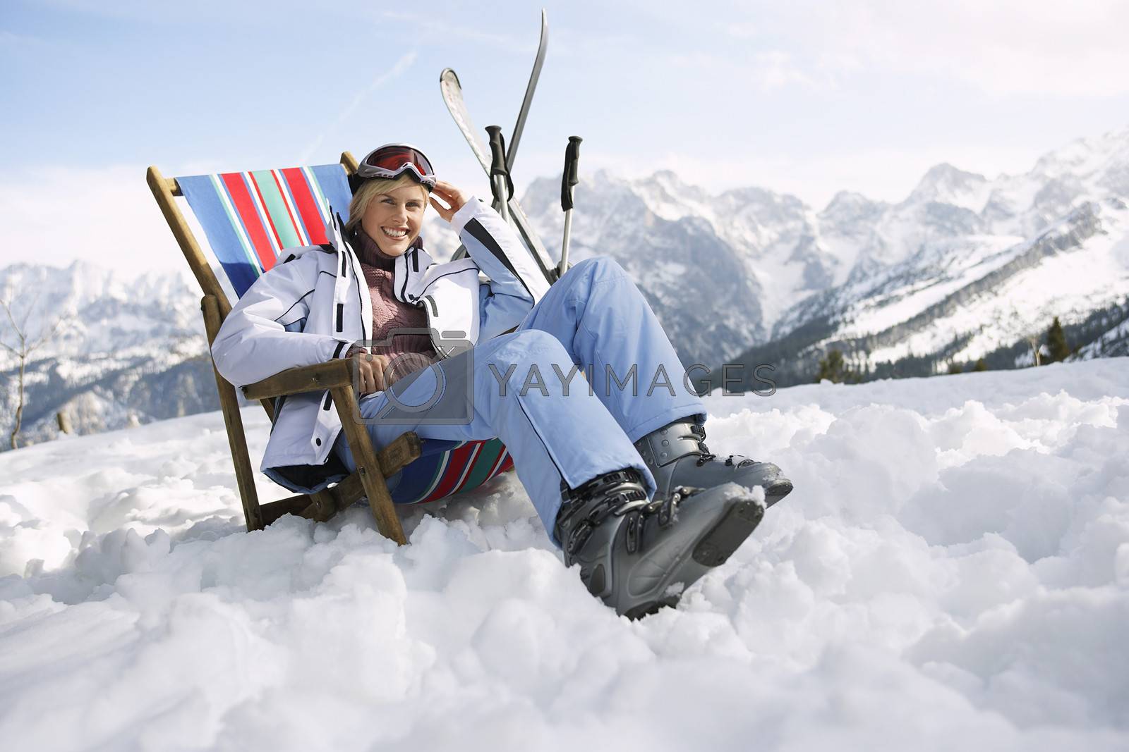 Royalty free image of Portrait of a smiling woman sitting on deckchair in snowy mountains by moodboard