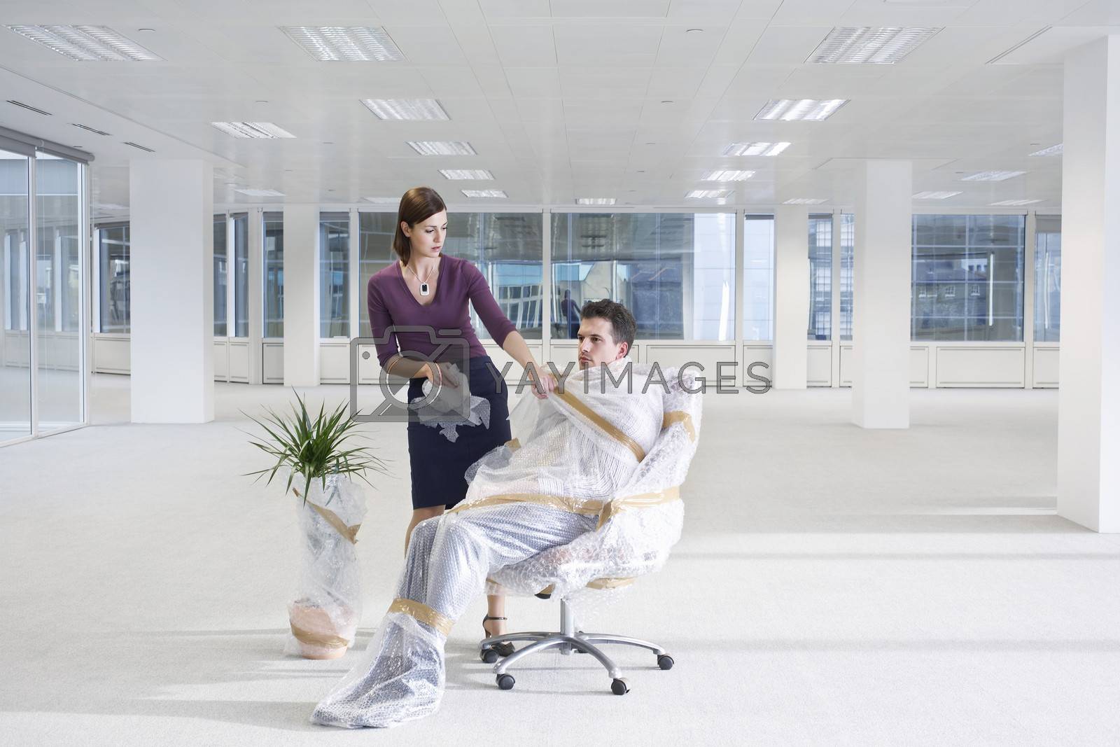 Royalty free image of Secretary unwrapping businessman on chair in empty office space by moodboard