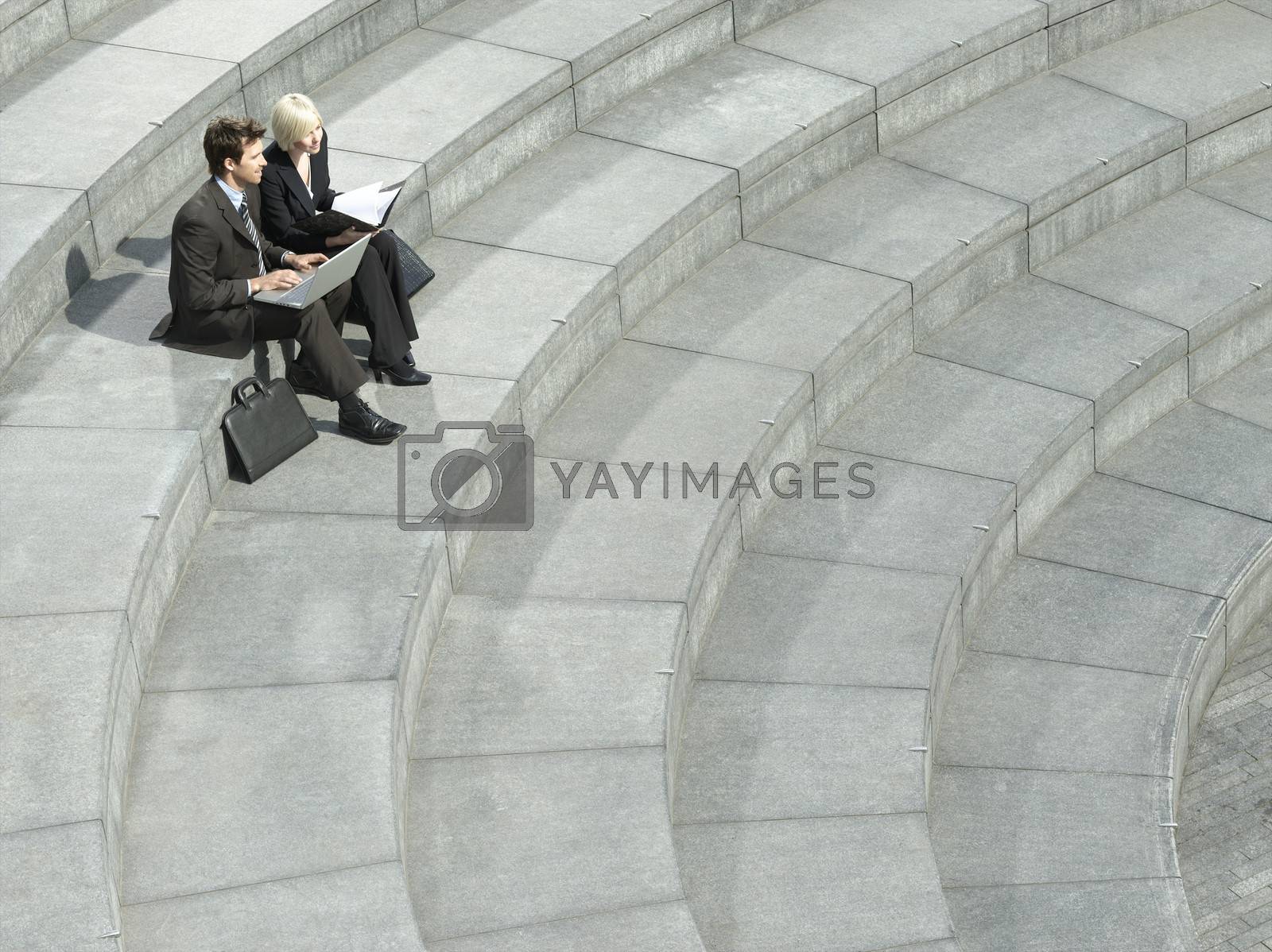 Royalty free image of Business man and woman sitting on spiral stairs using laptop elevated view by moodboard