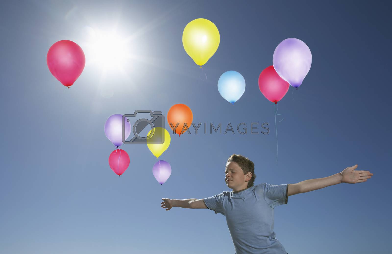 Royalty free image of Carefree elementary boy in midair with colorful balloons against blue sky by moodboard