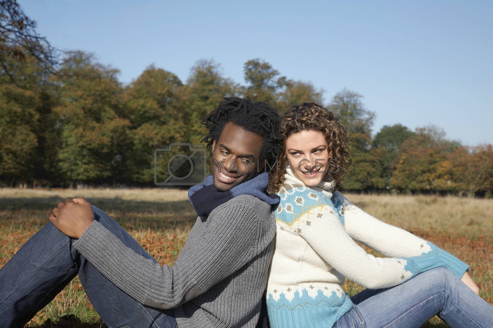 Royalty free image of Couple sitting back to back in field side view by moodboard