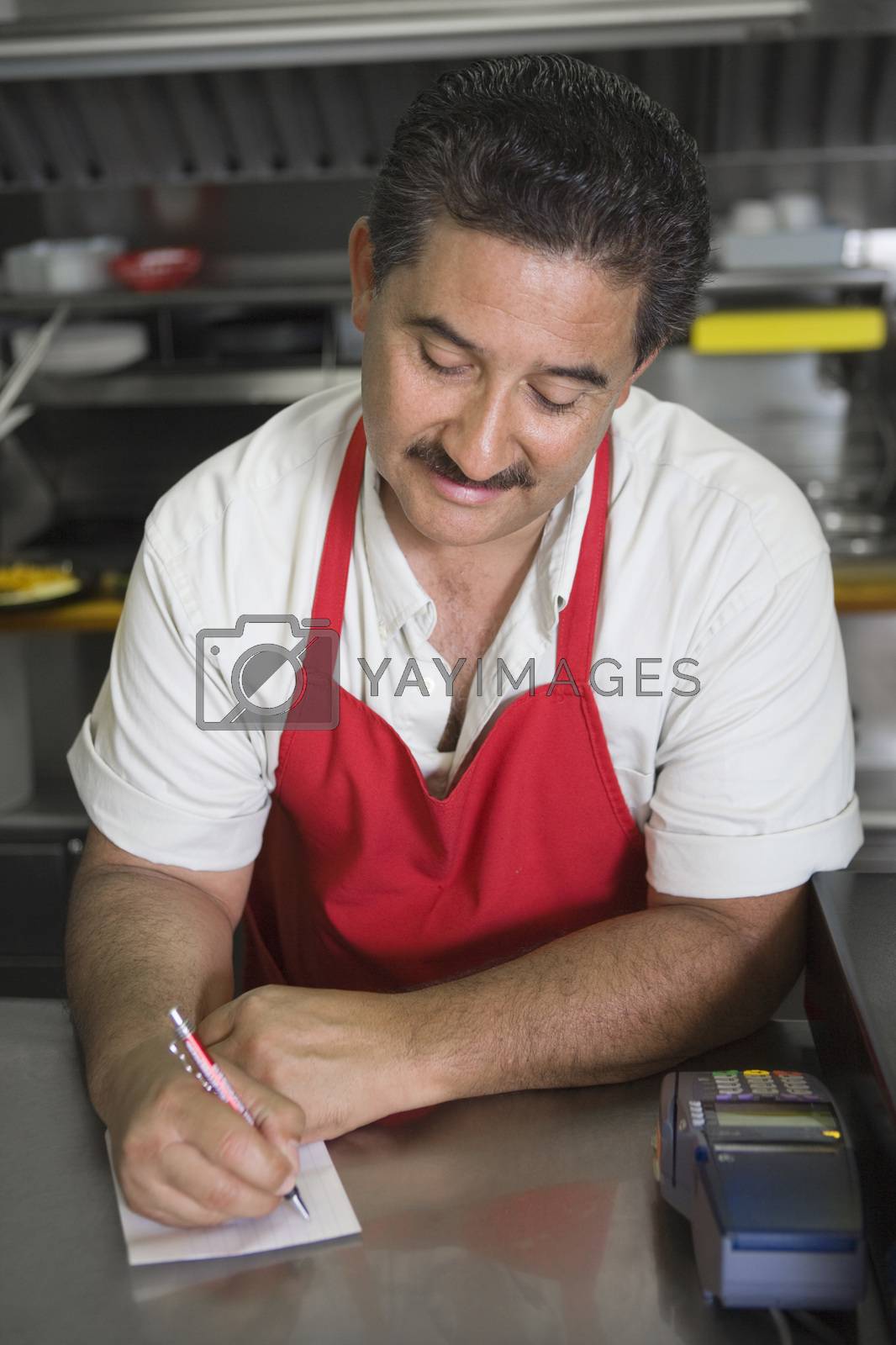 Royalty free image of Hispanic Latin man writing an order while standing at counter in restaurant by moodboard
