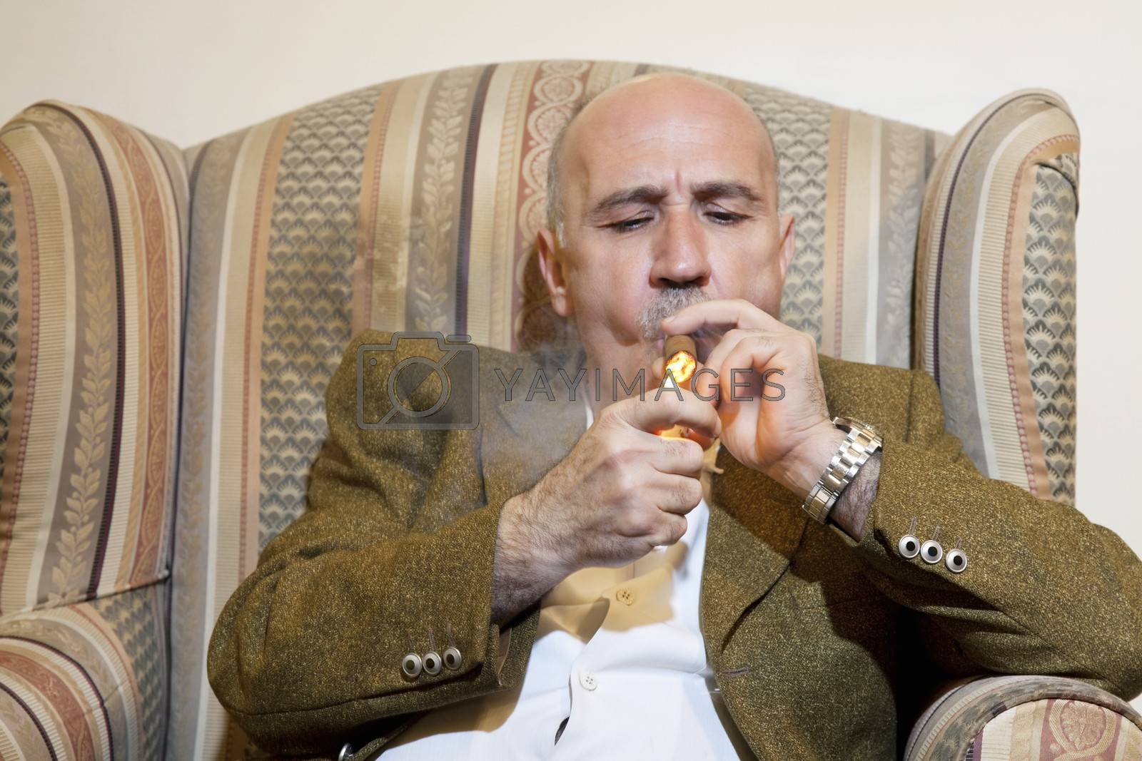 Royalty free image of Mature man igniting cigar while sitting on armchair by moodboard