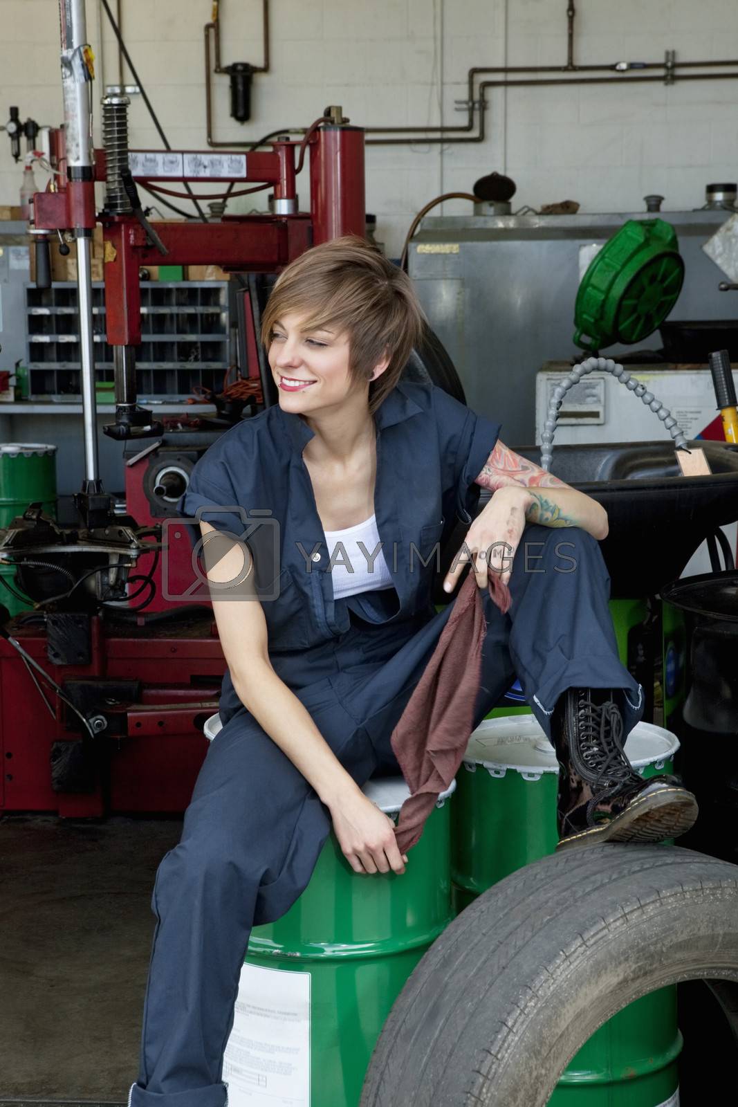 Royalty free image of Happy young female mechanic sitting on oil drum in automobile repair shop by moodboard