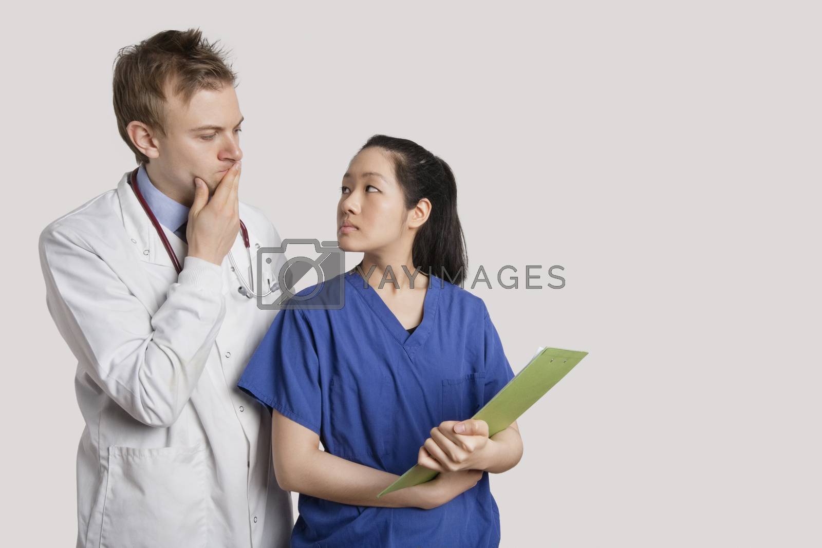 Royalty free image of Serious Caucasian doctor and Asian nurse looking at each other over gray background by moodboard