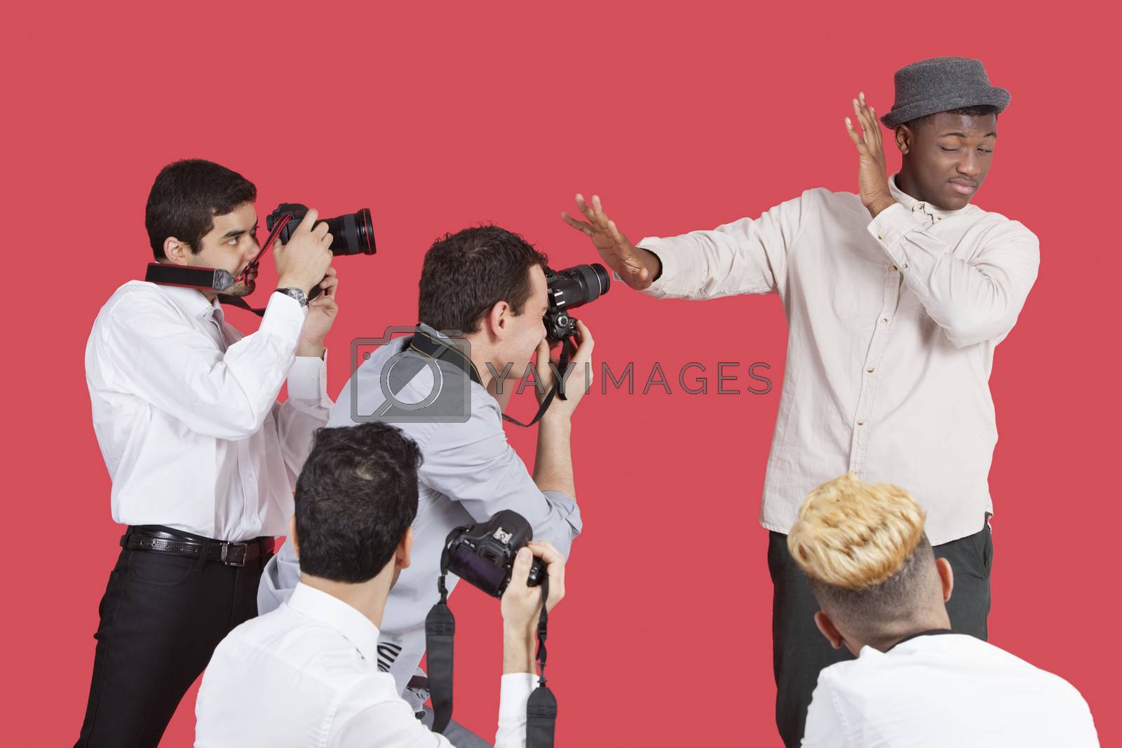 Royalty free image of Young male celebrity shielding face from photographers over red background by moodboard