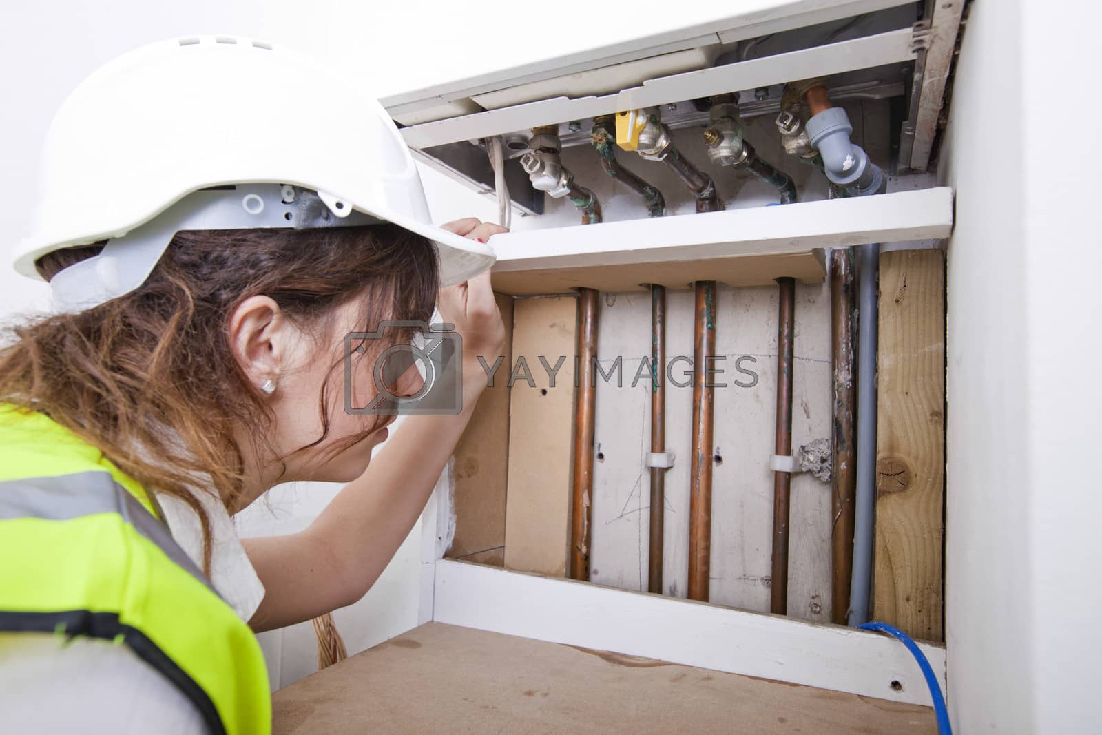 Royalty free image of Female plumber examining pipes of central heating boiler by moodboard