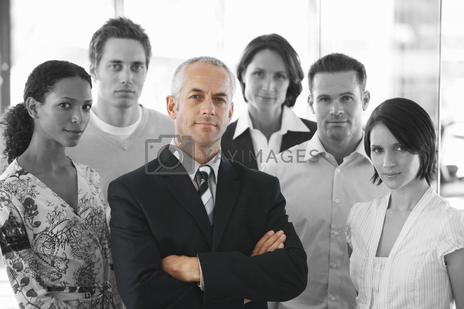 Royalty free image of Portrait of a confident businessman standing arms crossed with office workers by moodboard