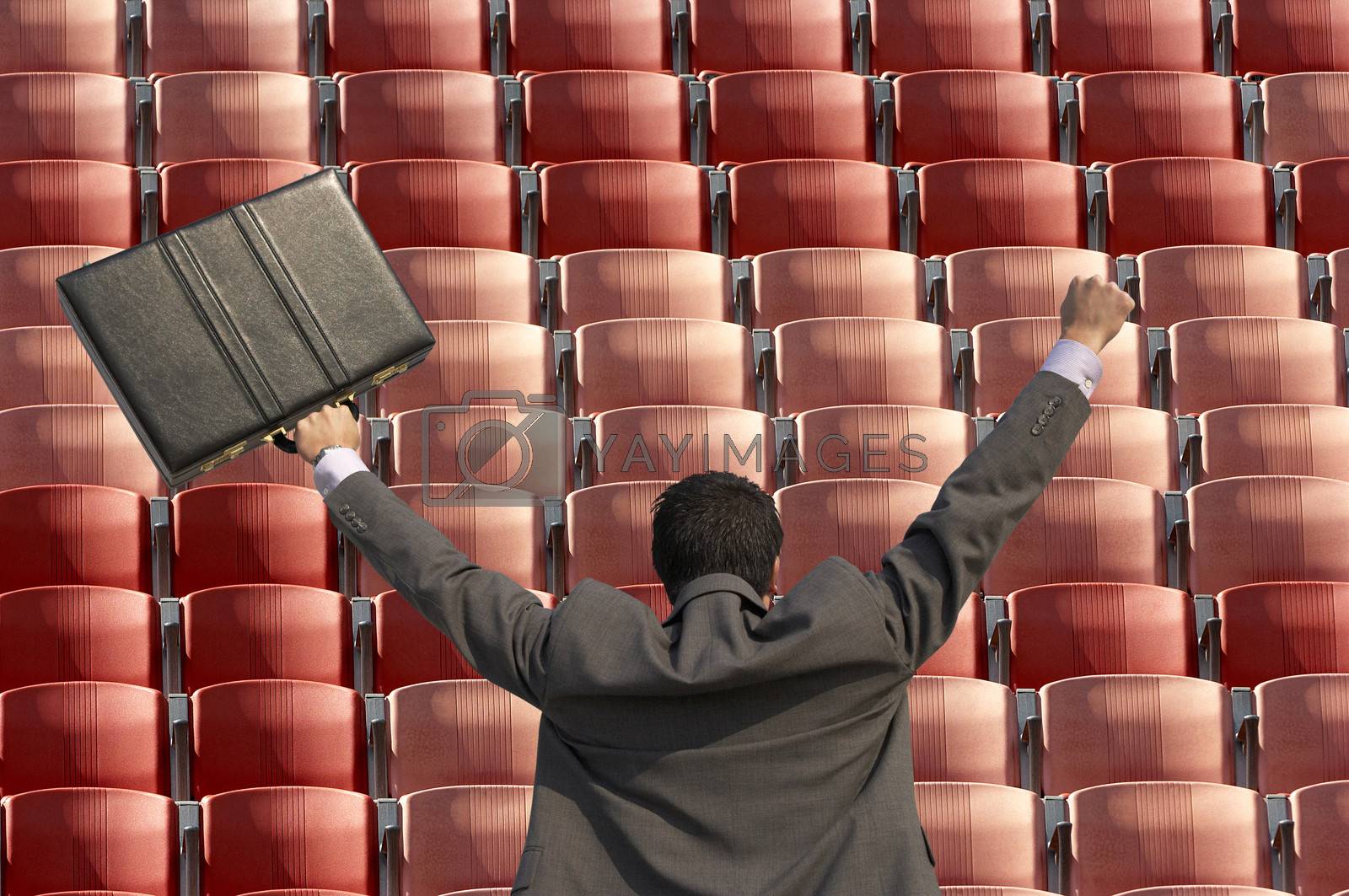 Royalty free image of Back view of victorious businessman with briefcase facing rows of red seats at stadium by moodboard