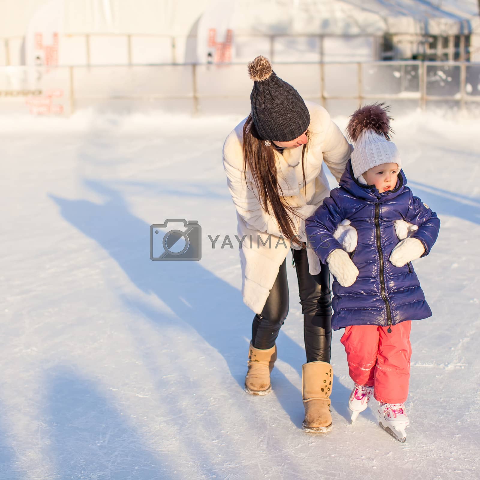 Royalty free image of Happy excited little girl and her young mother learning ice-skating by travnikovstudio
