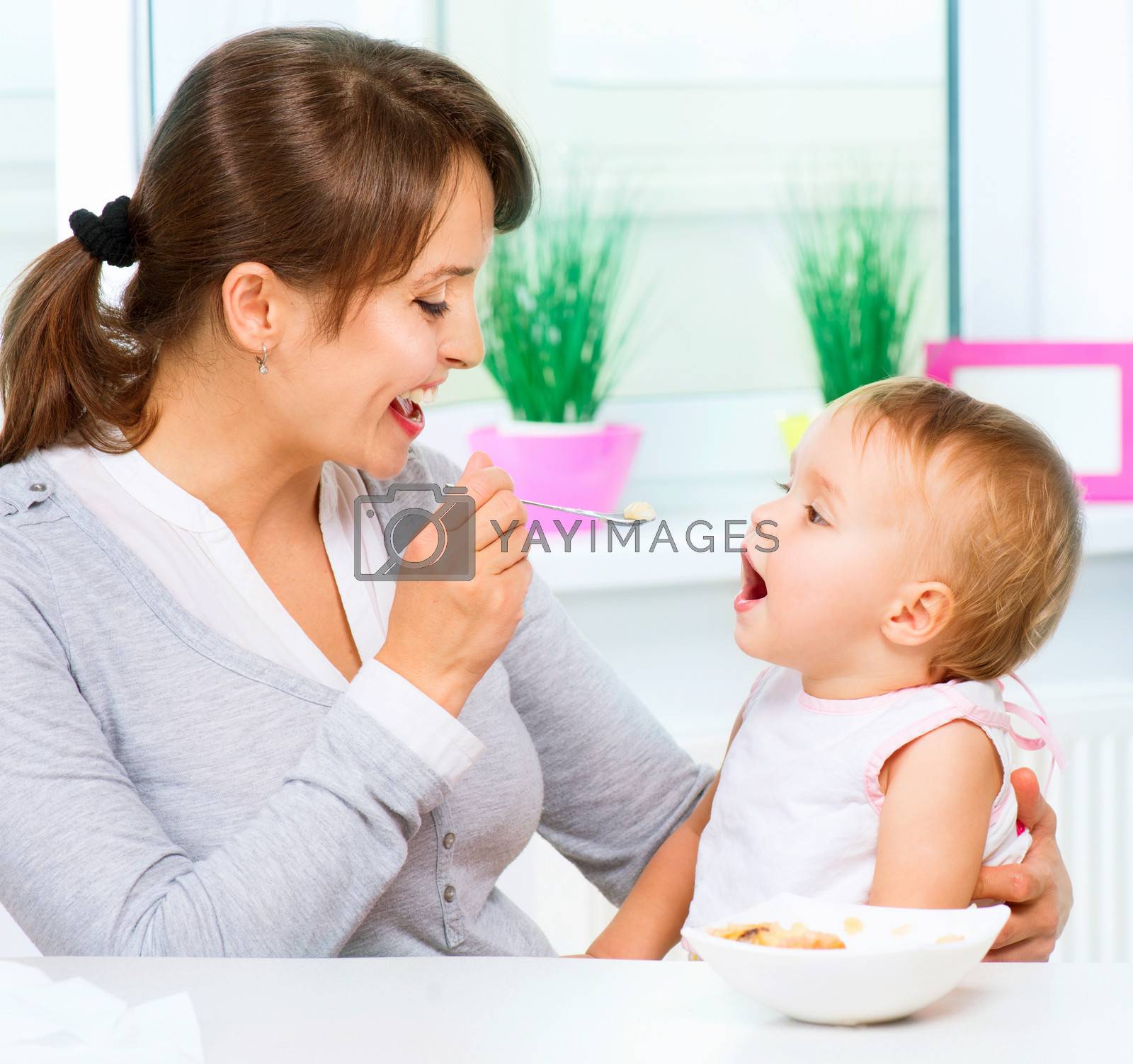 Royalty free image of Mother Feeding Her Baby Girl with a Spoon by SubbotinaA