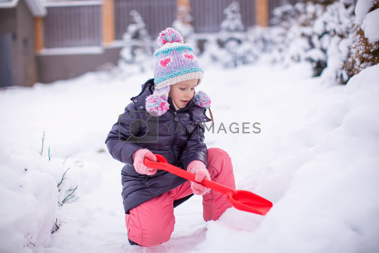 Royalty free image of Little adorable girl play with snow shoveling on a winter day by travnikovstudio