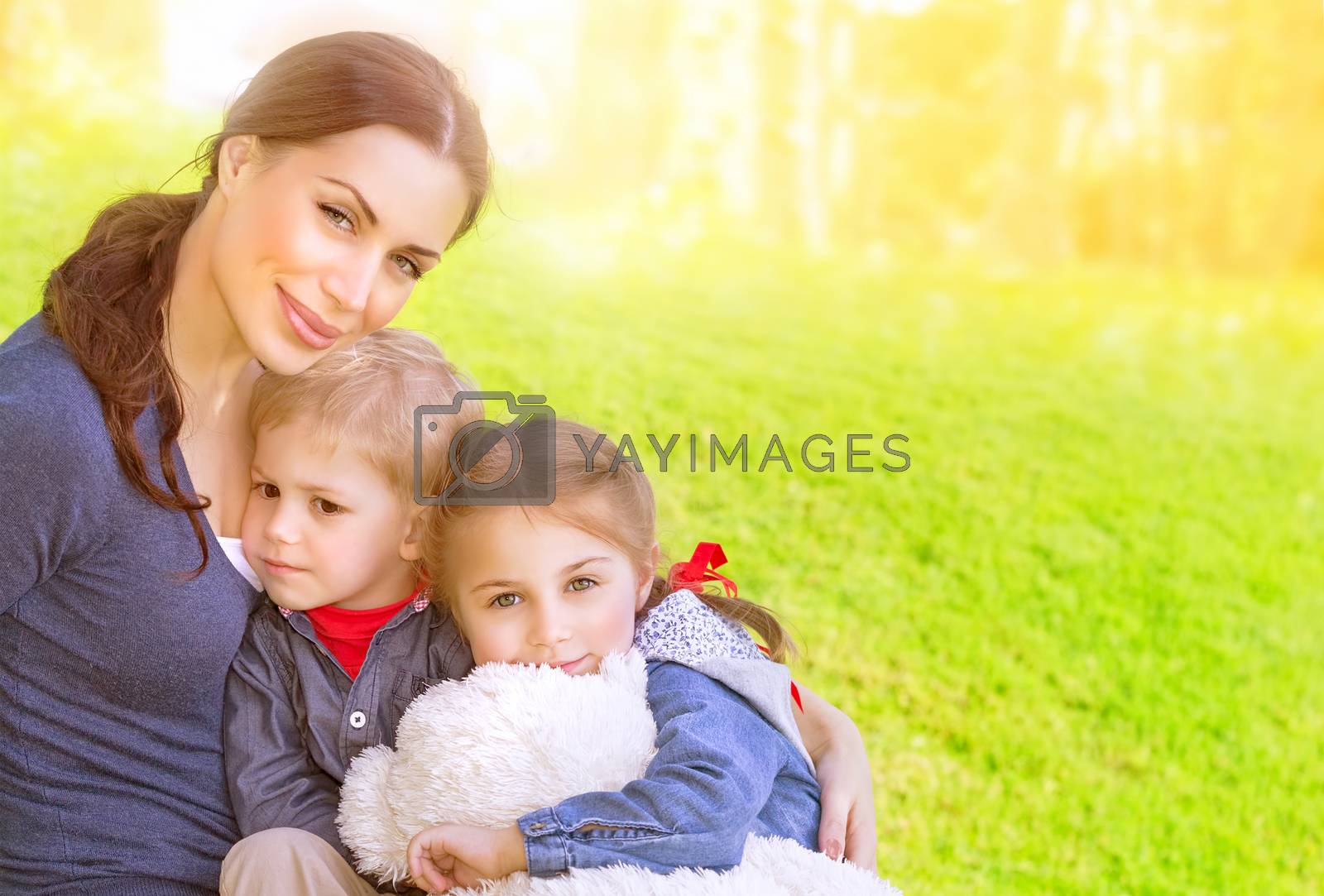  Portrait of beautiful young mother with cute daughter and son sitting on the meadow, sunny day, love and happy family concept