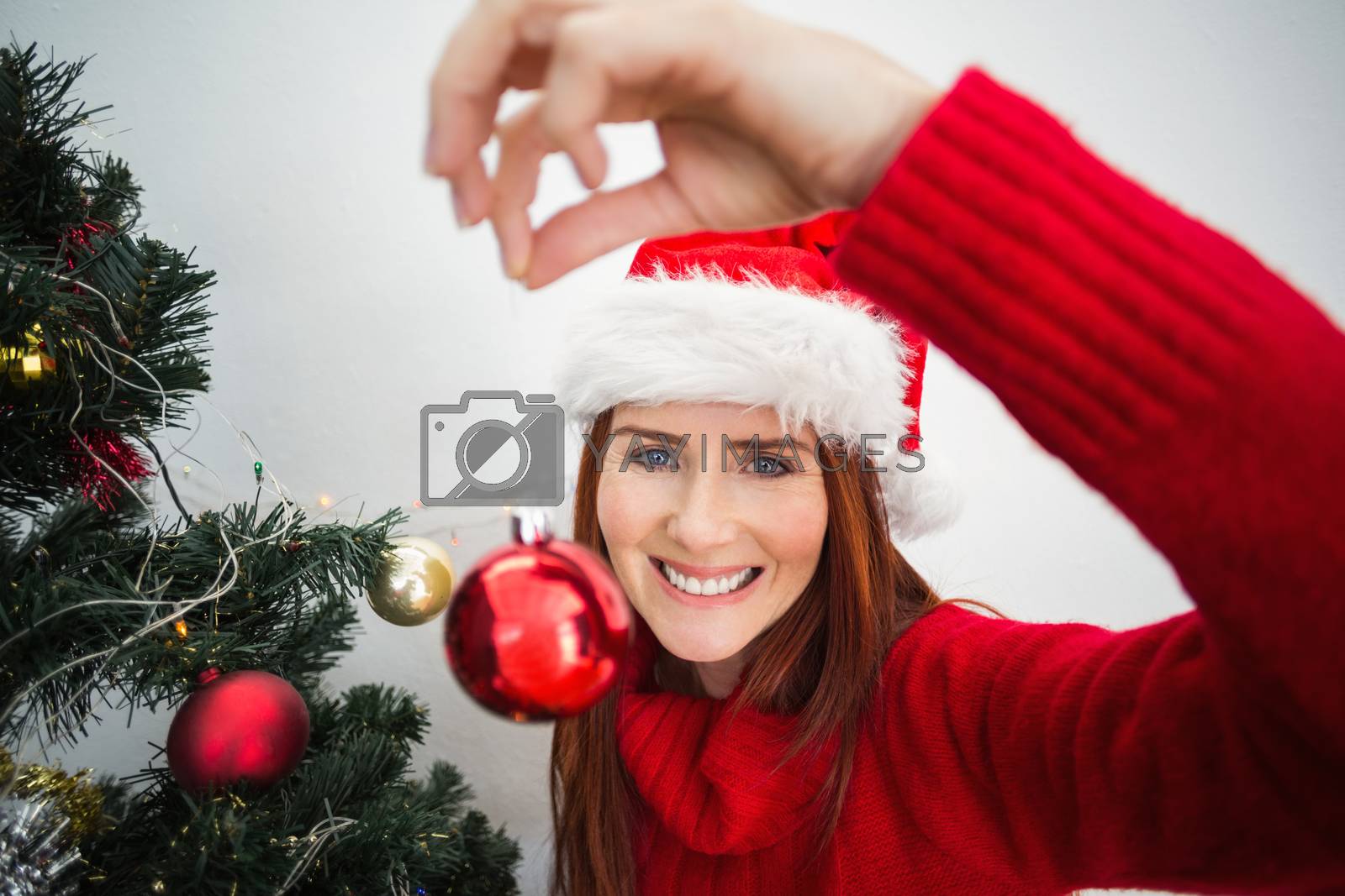 Royalty free image of Festive redhead hanging bauble on tree by Wavebreakmedia