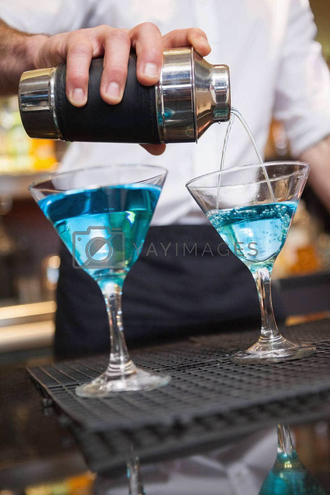 Royalty free image of Bartender pouring cocktail into glasses by Wavebreakmedia