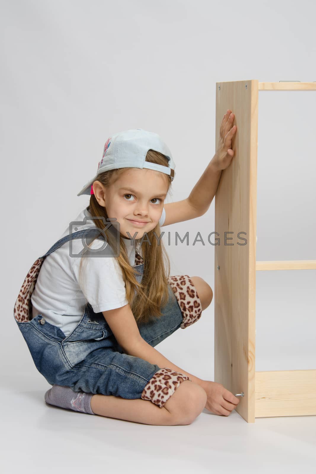 Royalty free image of Little girl in overalls collector of furniture turn screw on dresser by Madhourse