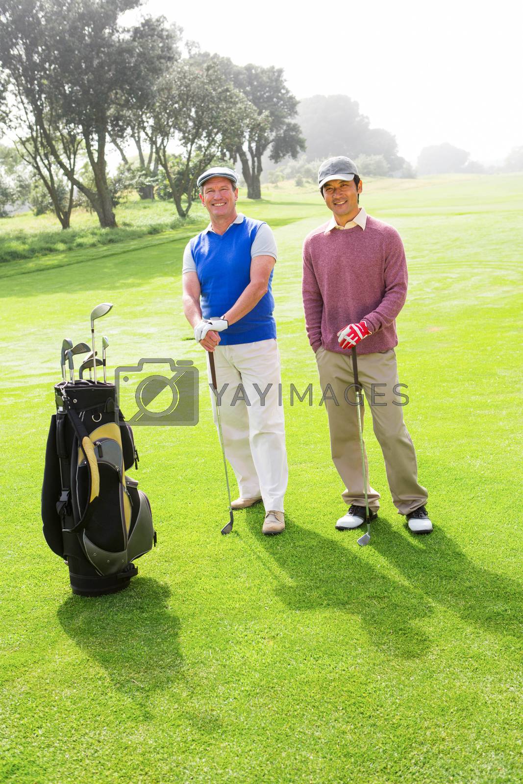Royalty free image of Golfing friends smiling at camera holding clubs by Wavebreakmedia