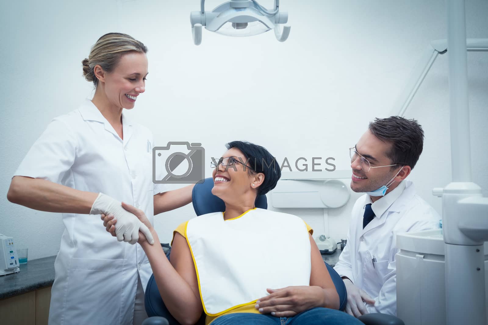 Royalty free image of Male dentist with assistant shaking hands with woman by Wavebreakmedia