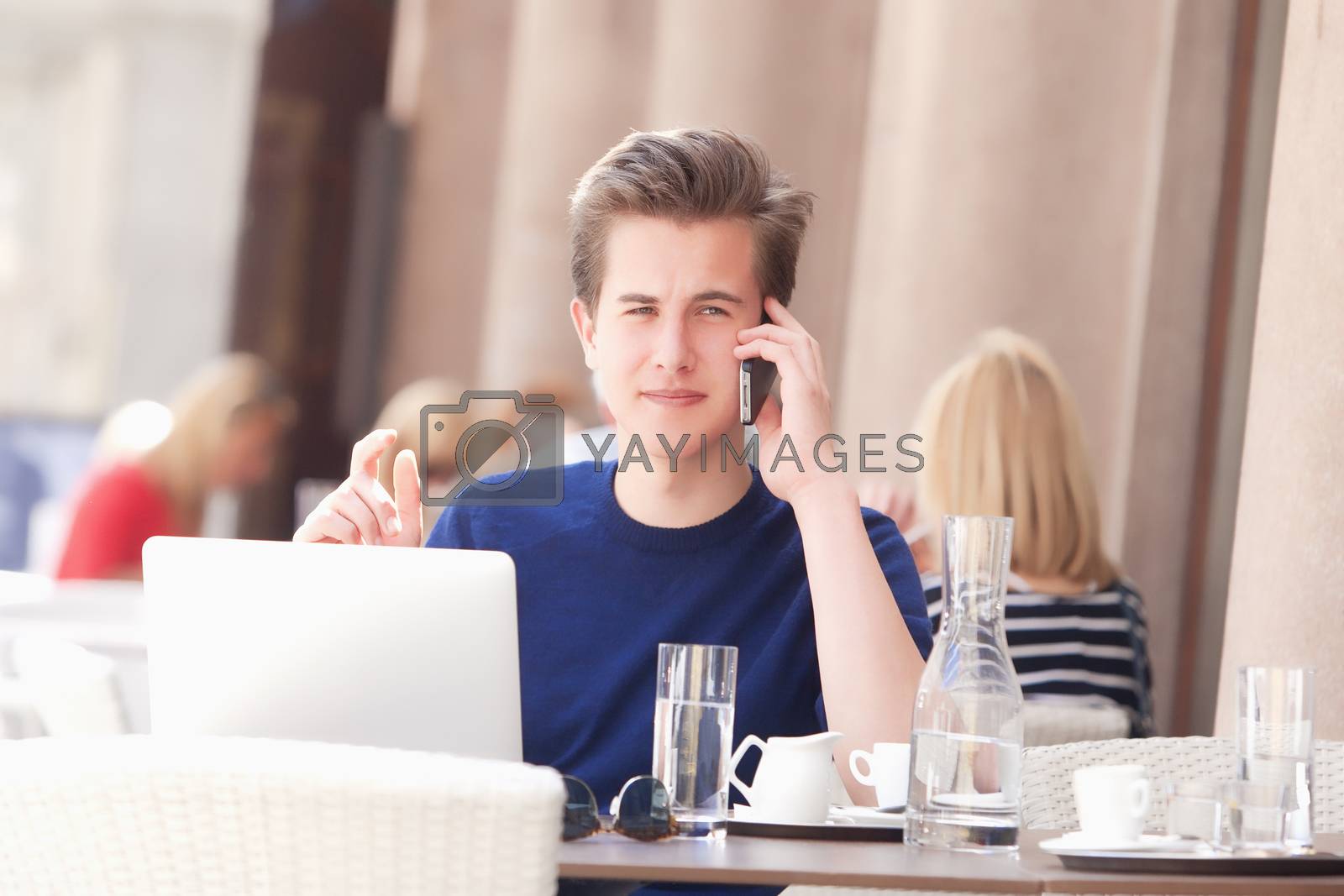 Royalty free image of Young Man Sitting in Outside Coffeehouse Talking on Phone by courtyardpix