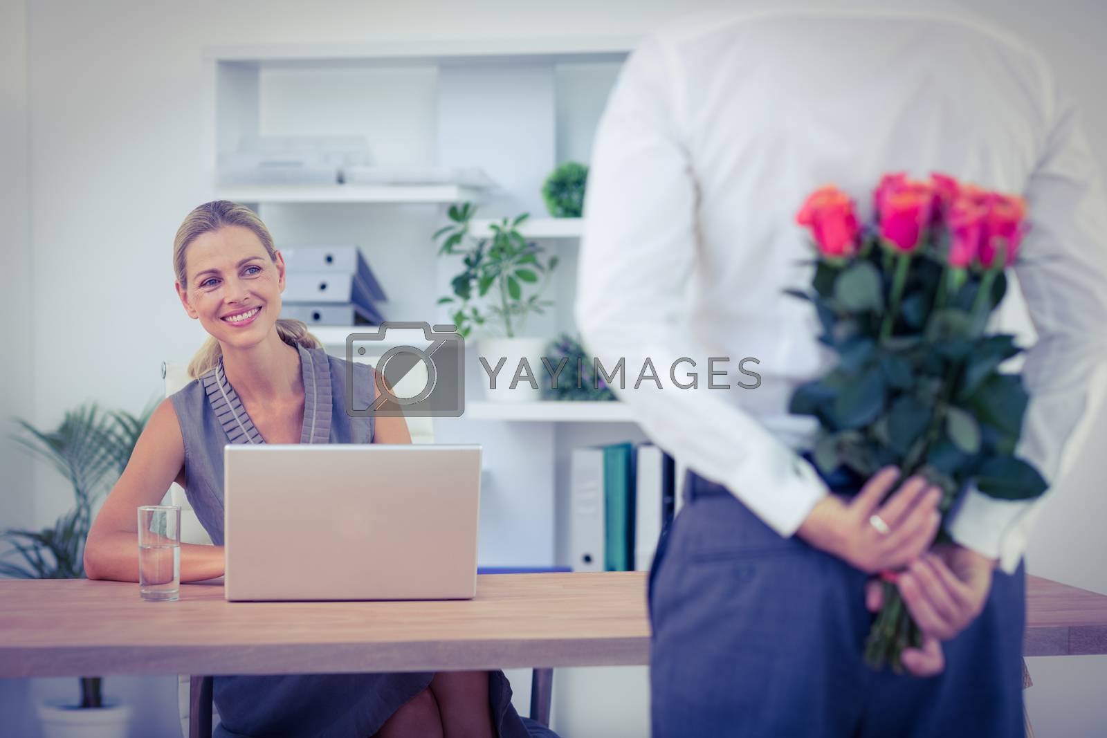 Royalty free image of Man hiding bouquet in front of businesswoman at desk by Wavebreakmedia