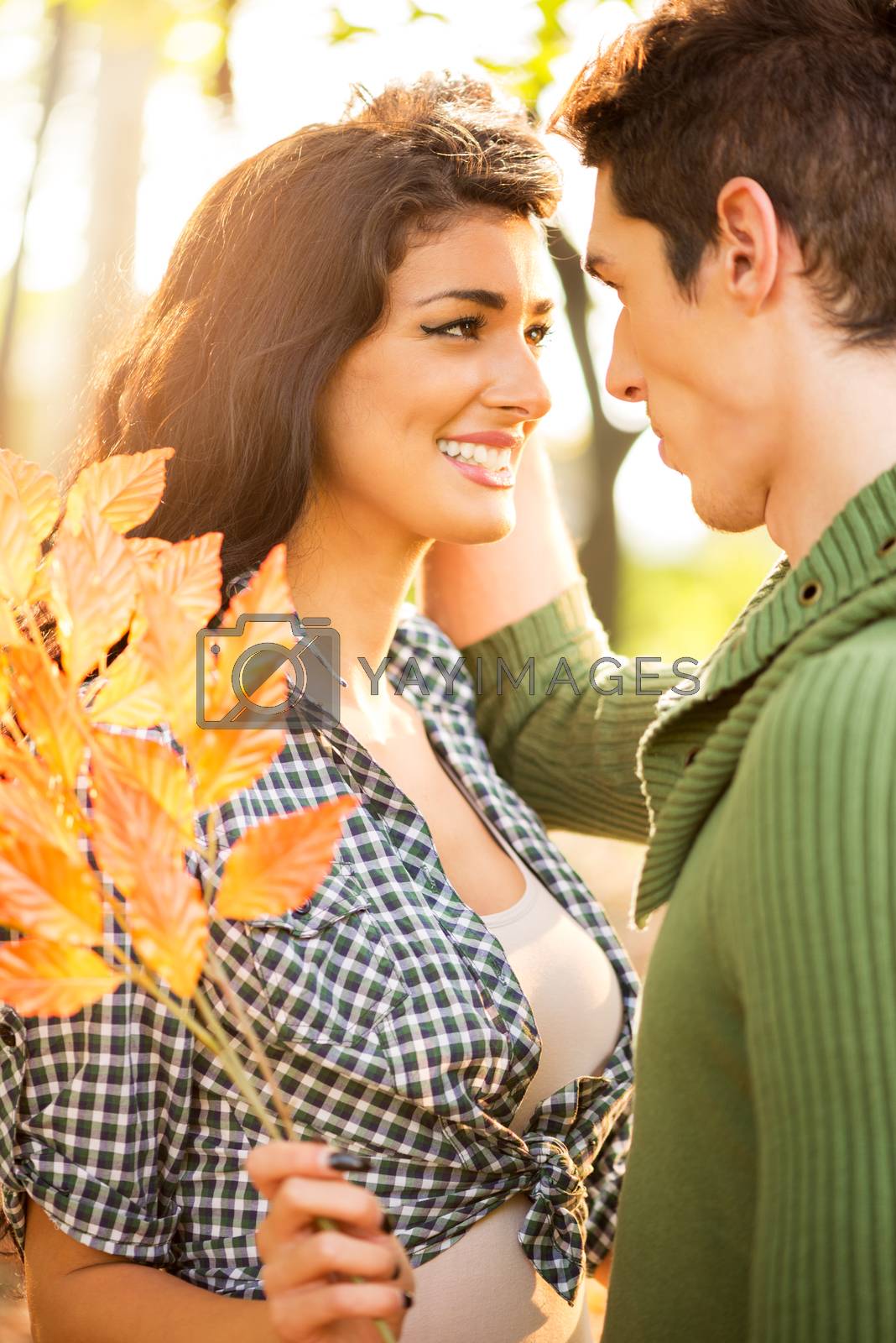Smiling pretty girl in the park is holding a sprig of autumn leaves and looking lovingly at her boyfriend.