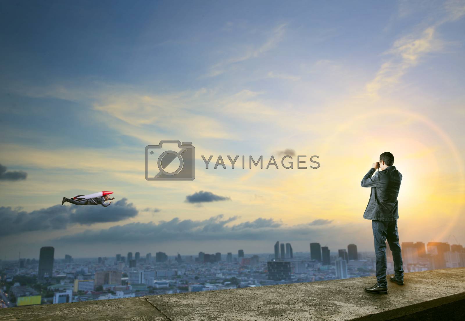 Royalty free image of business man binocular to man with rocket on back flying over ci by khunaspix