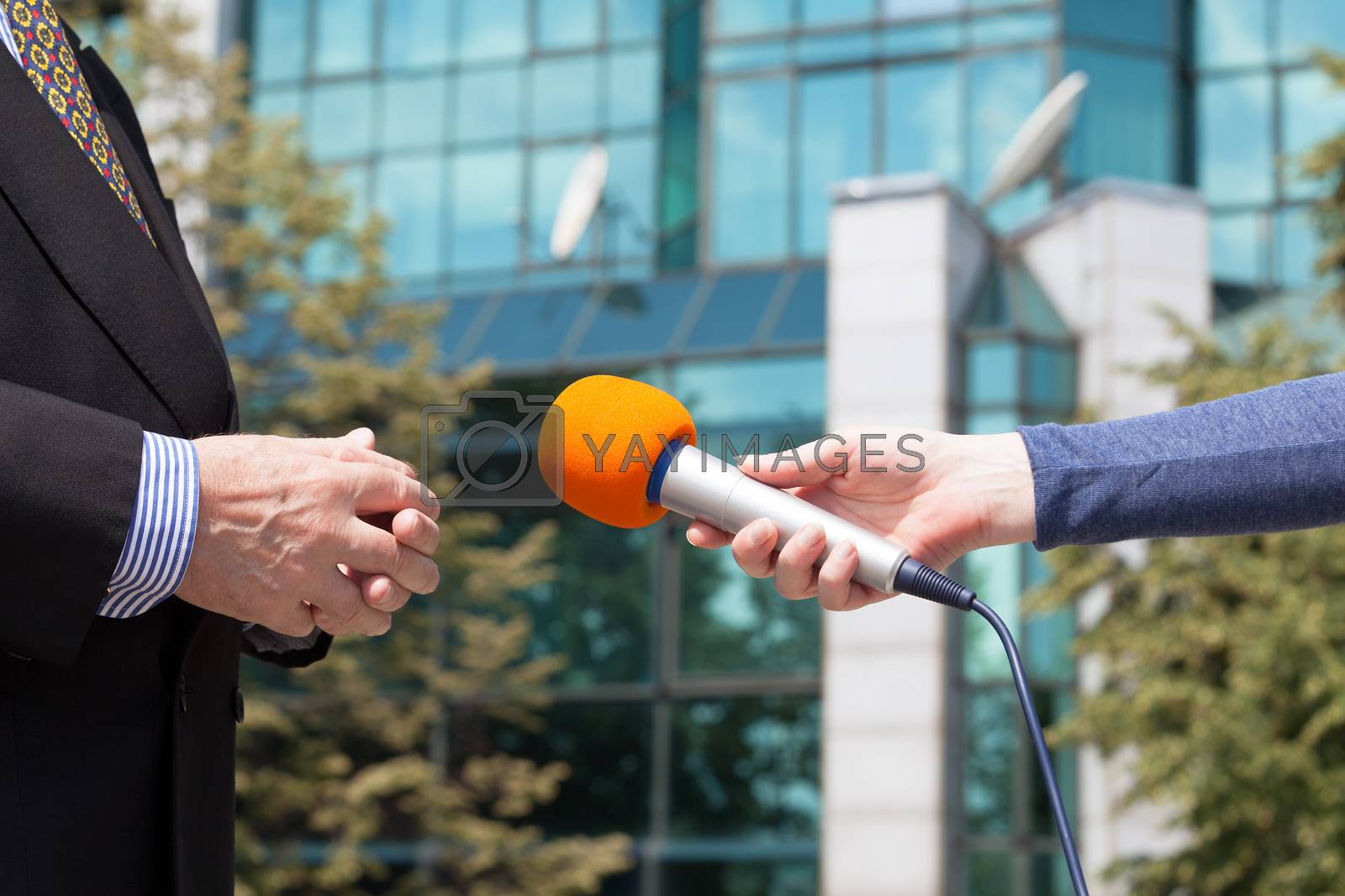 Royalty free image of Reporter interviewing businessman, corporate building in background by wellphoto