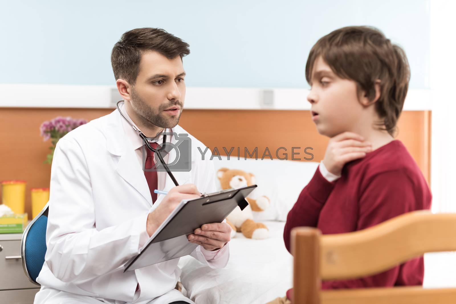 Royalty free image of Man doctor with clipboard examining child patient with sore throat by LightFieldStudios