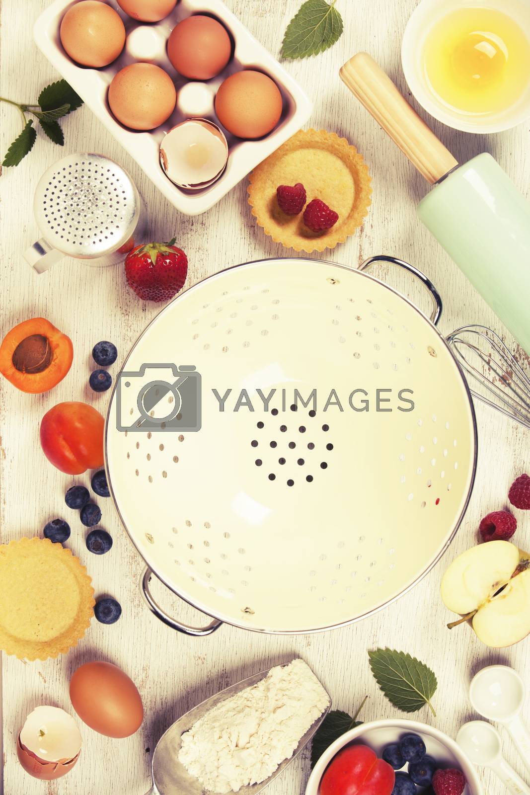 Antique colander, Baking tools and ingredients - flour, rolling pin, eggs, measuring spoons, fruits and berries on vintage wood table. Top view. Rustic background with free text space
