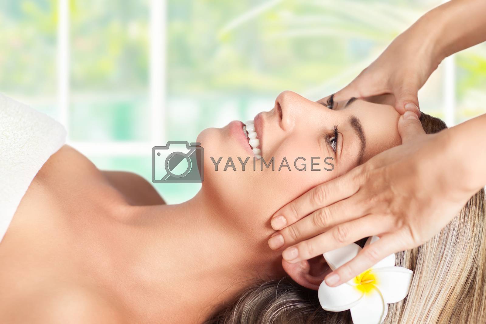 Beautiful blond woman lying down on massage table in spa salon, enjoying facial massage, doing facial mask, healthy lifestyle and beauty treatment concept