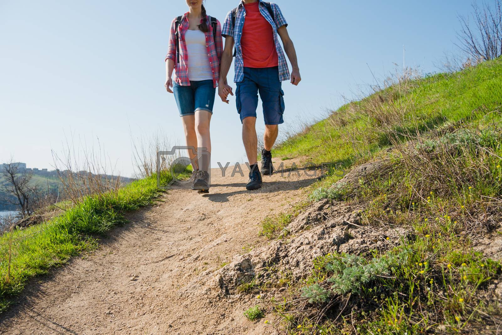Royalty free image of Young Couple Hiking with Backpacks on the Beautiful Rocky Trail at Sunny Evening. Family Travel and Adventure. by maxpro