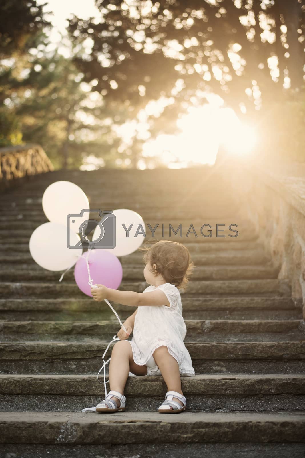 Royalty free image of Baby girl standing on stairs and holding balloons. Vintage looking. Sun, sun haze, glare by sevda_stancheva