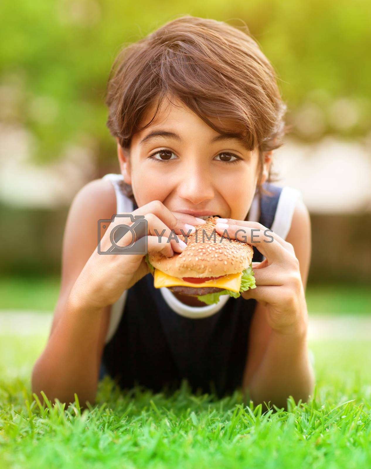 Royalty free image of Teen boy eating burger outdoors by Anna_Omelchenko